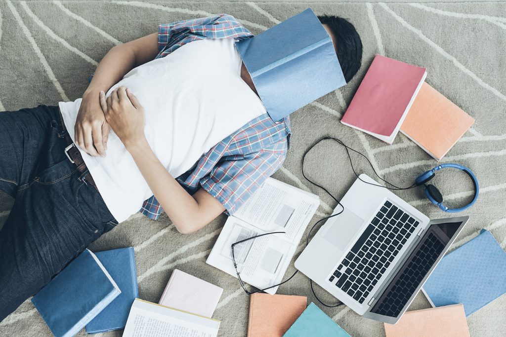 Uma imagem contendo um homem deitado, quatro livros e um computador
